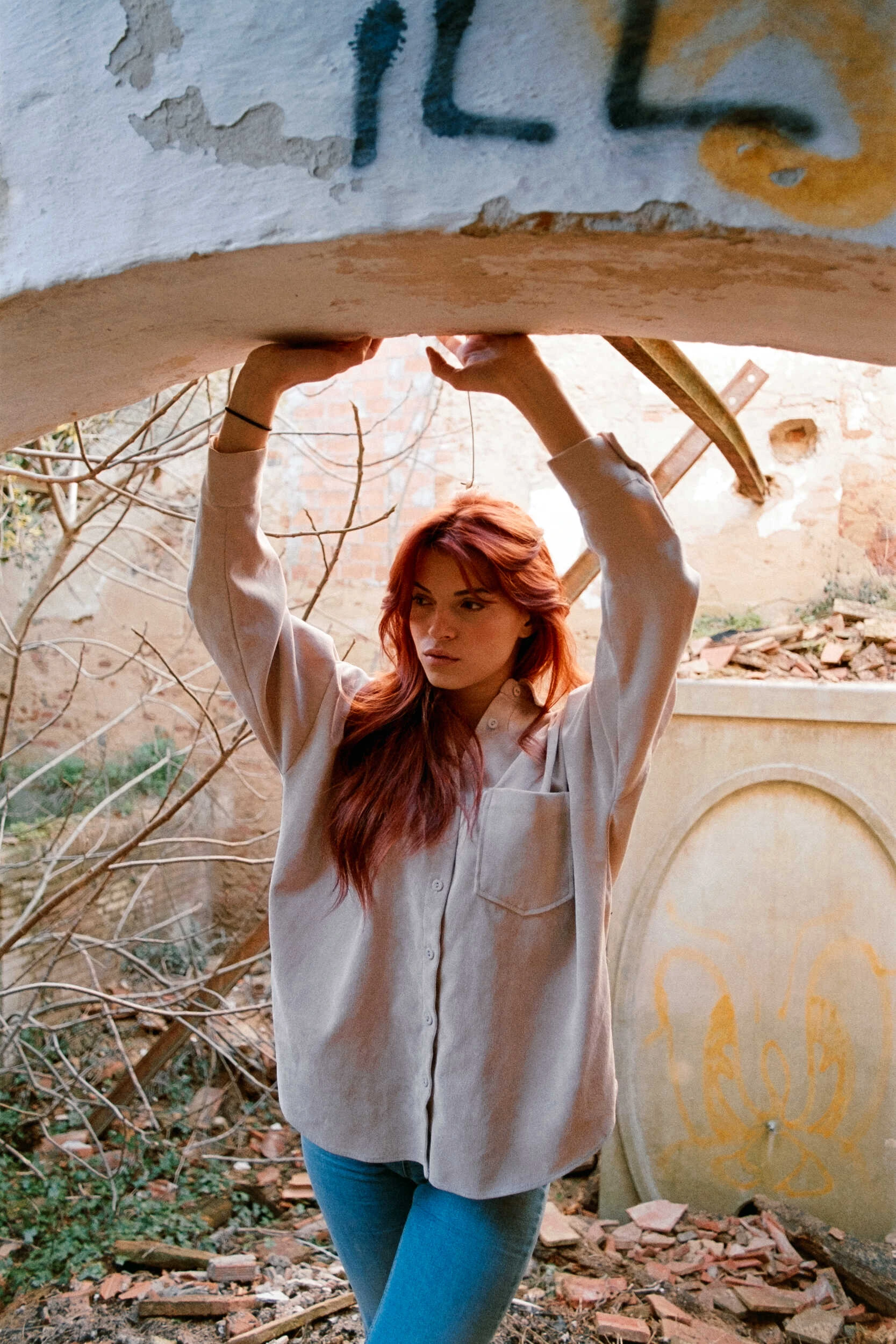 Red-haired model under a graffiti arch with a raised arm, analog film portrait in Tuscany