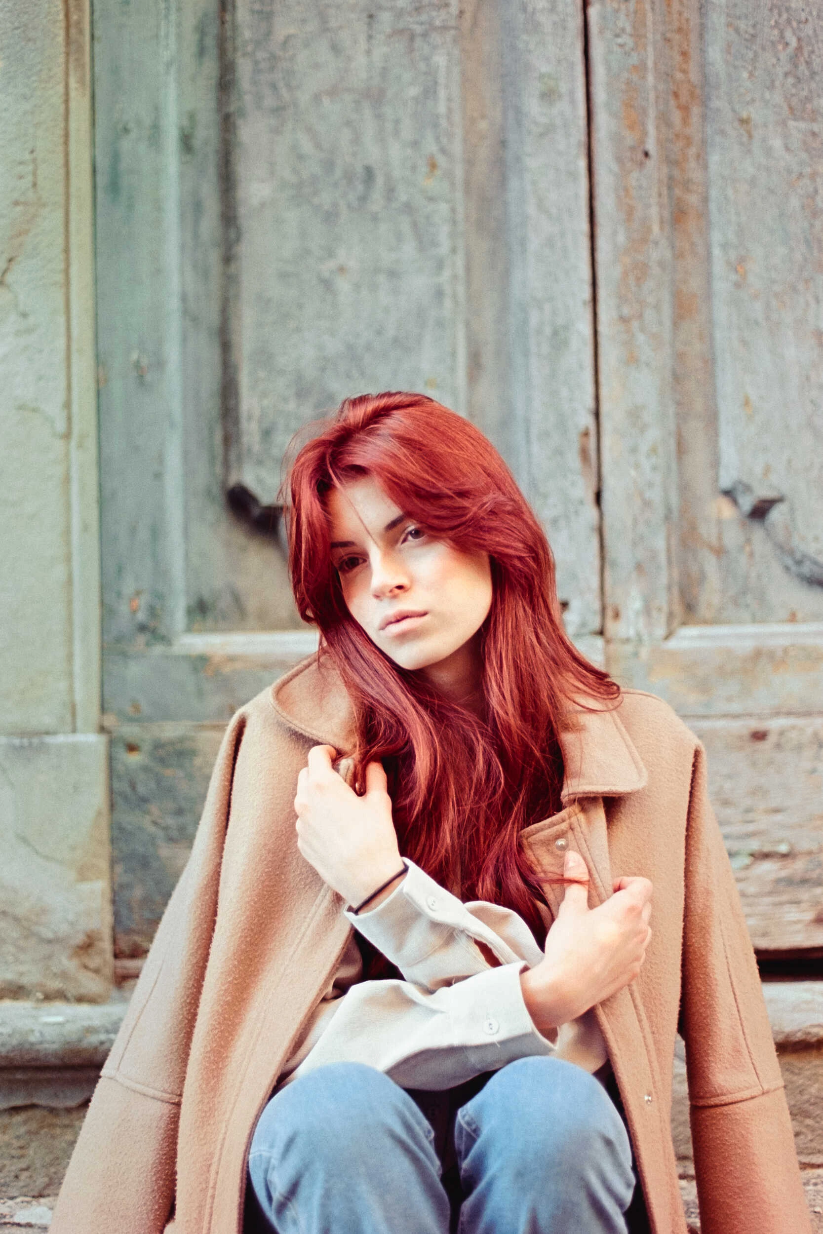 Red-haired model in a camel coat with a hand in her hair, analog film portrait in Tuscany