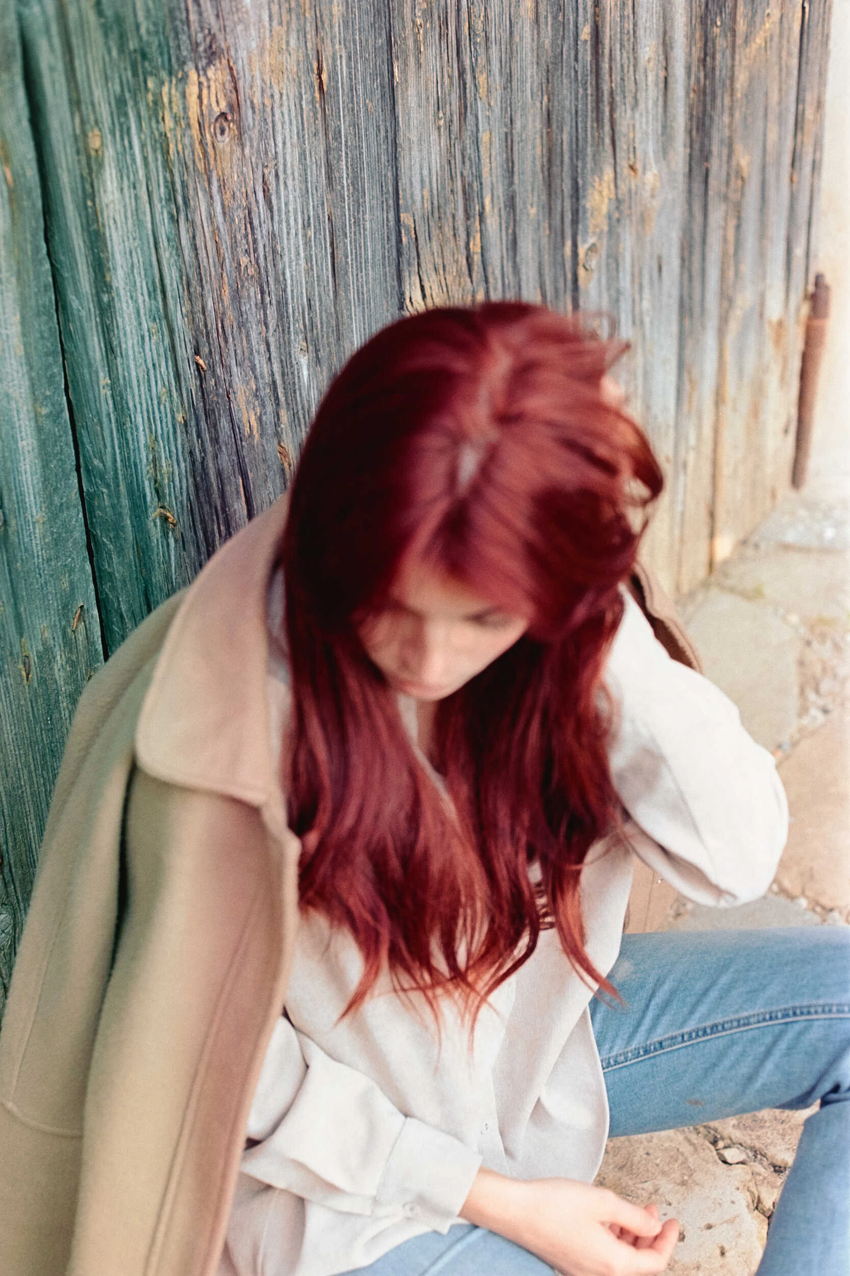Red-haired model in a camel coat looking down, analog film portrait in Tuscany