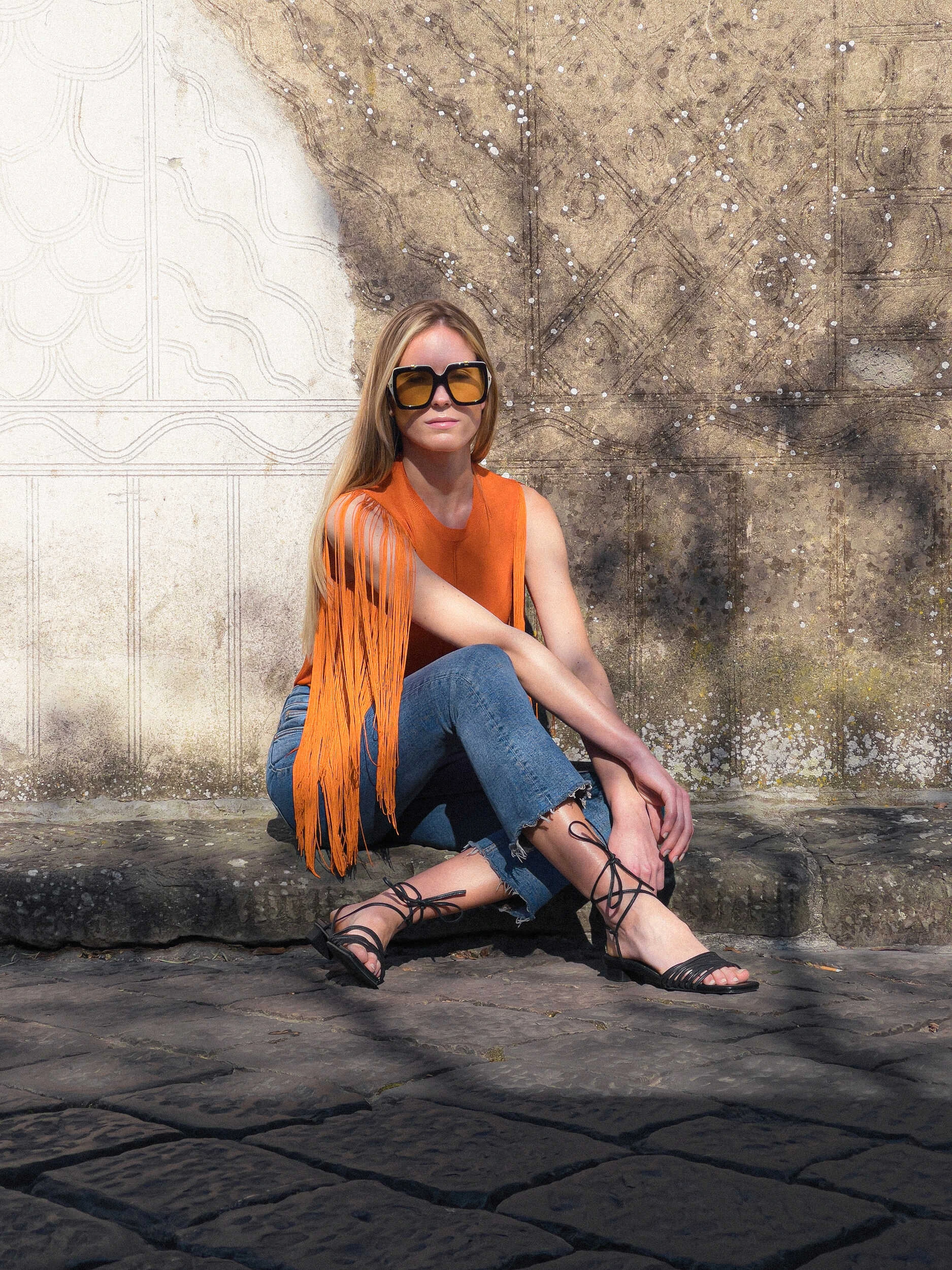 Blonde model in an orange fringed top and jeans crouching in Florence, hybrid photography