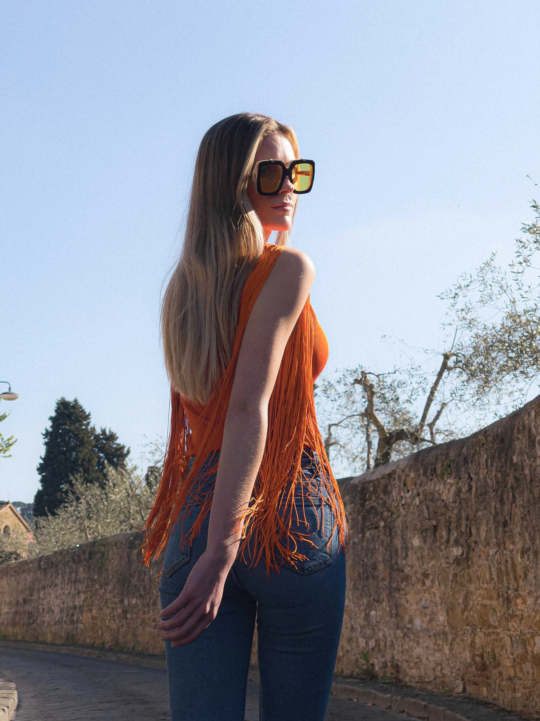 Blonde model in an orange fringed top and jeans standing in Florence, hybrid photography