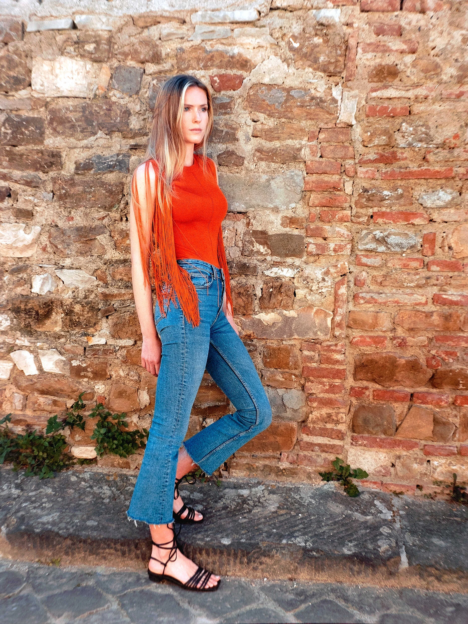 Blonde model in an orange top and jeans by a brick wall in Florence, hybrid photography