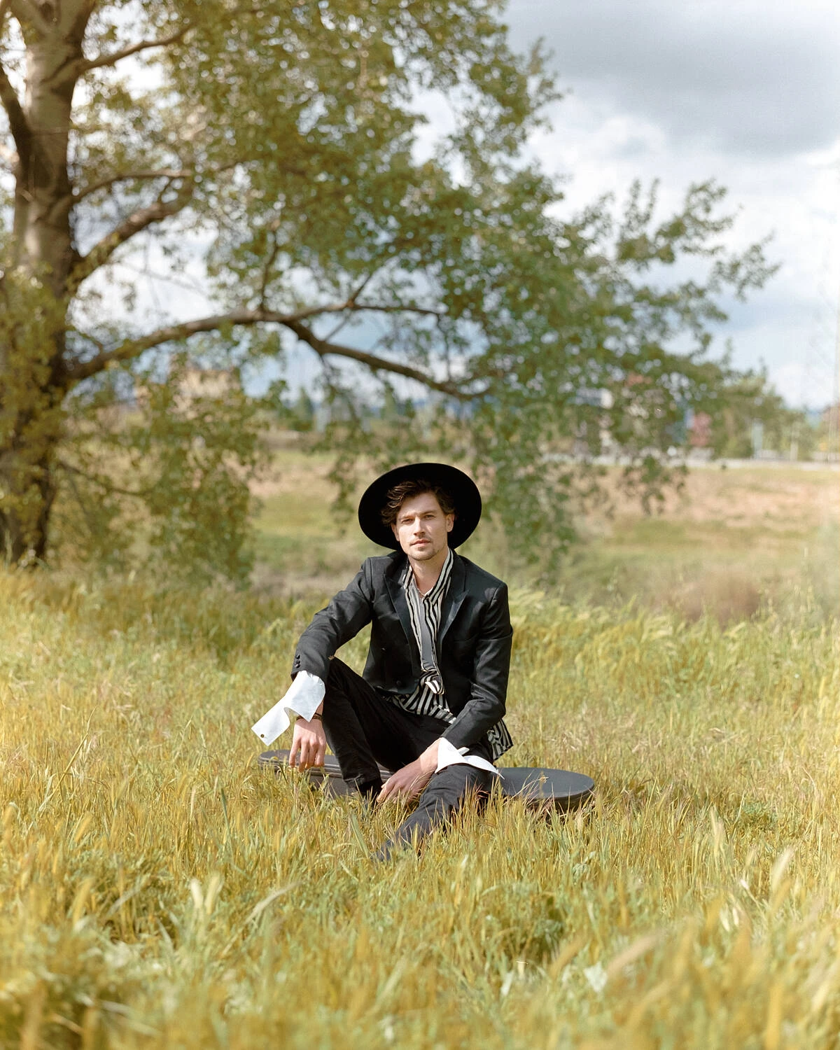 Robbie seated in a field in a black jacket and hat, shot on Fujifilm Pro 400H film