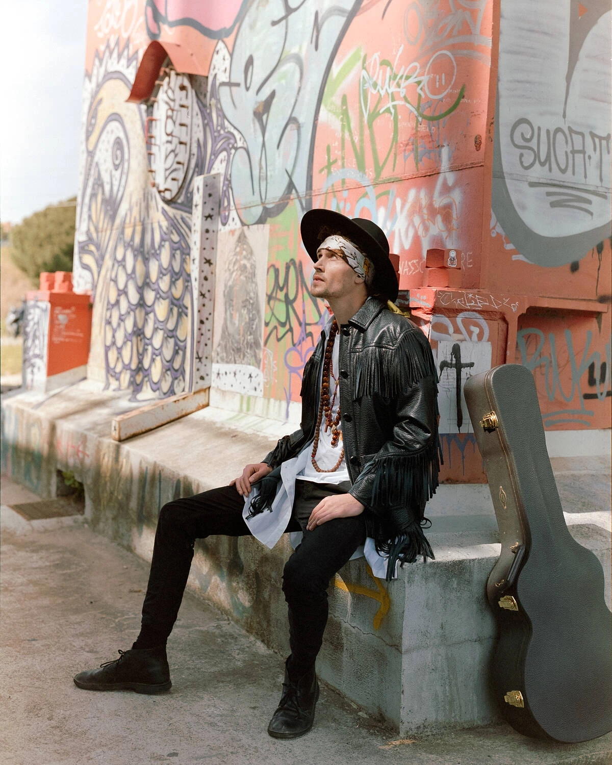 Robbie seated with a guitar case by a graffiti wall, shot on Fujifilm Pro 400H film