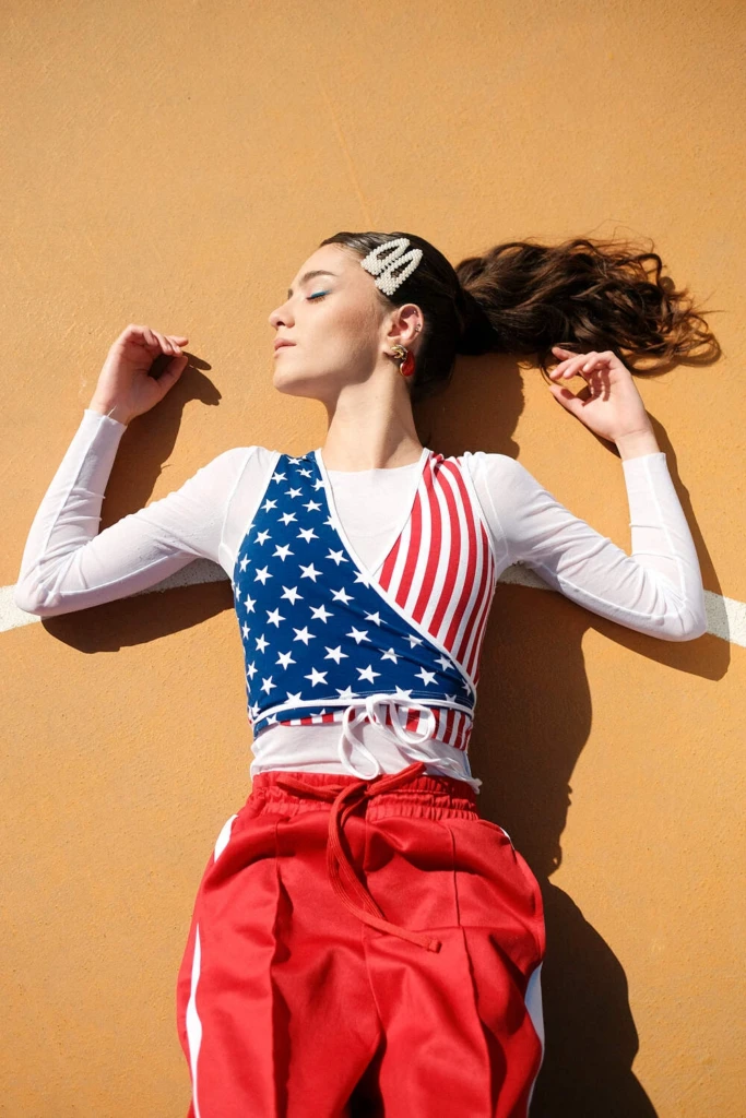 Chiara in an American-flag top and red trousers against an orange wall, shot on Fujifilm