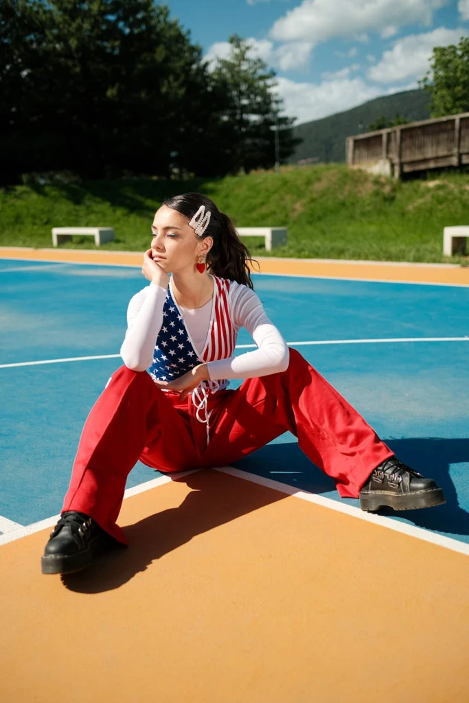 Chiara in an American-flag top and red trousers seated on a court, shot on Fujifilm