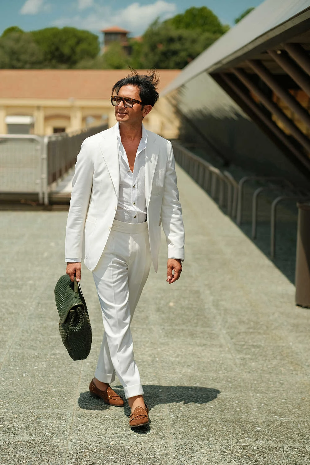 Man in a white suit walking a ramp with a bag, street style at Pitti Uomo 100 in Florence