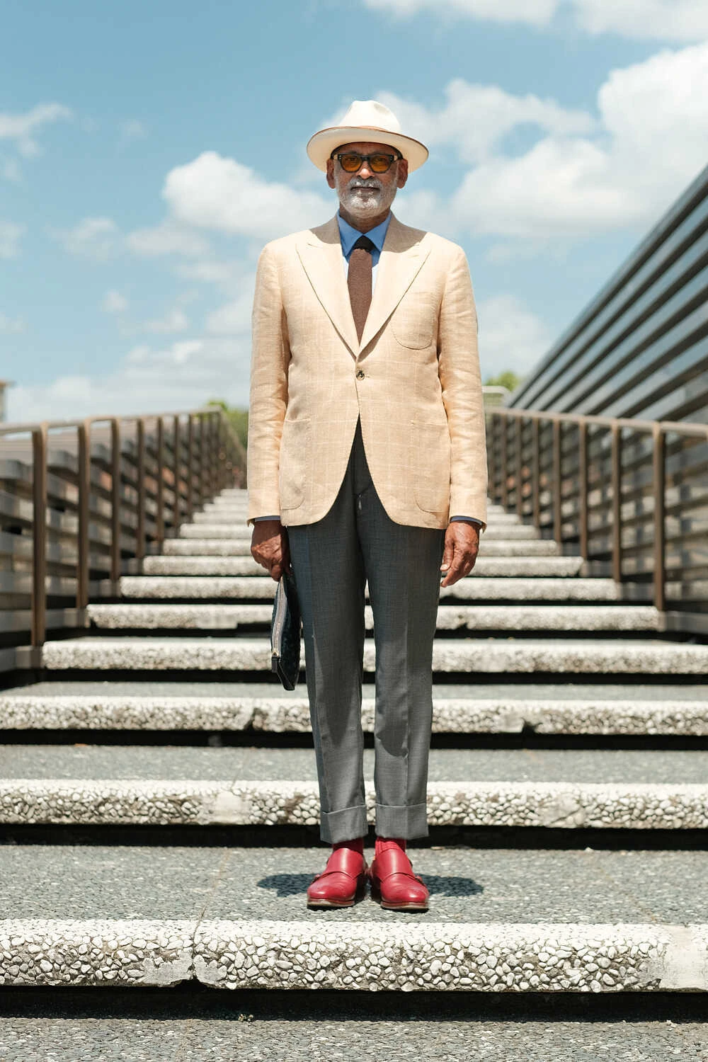 Man in a cream jacket and grey trousers with red boots on steps, street style at Pitti Uomo 100 in Florence
