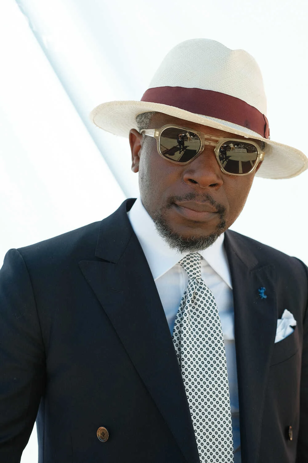Man in a navy suit and straw hat with a red band, street style at Pitti Uomo 100 in Florence
