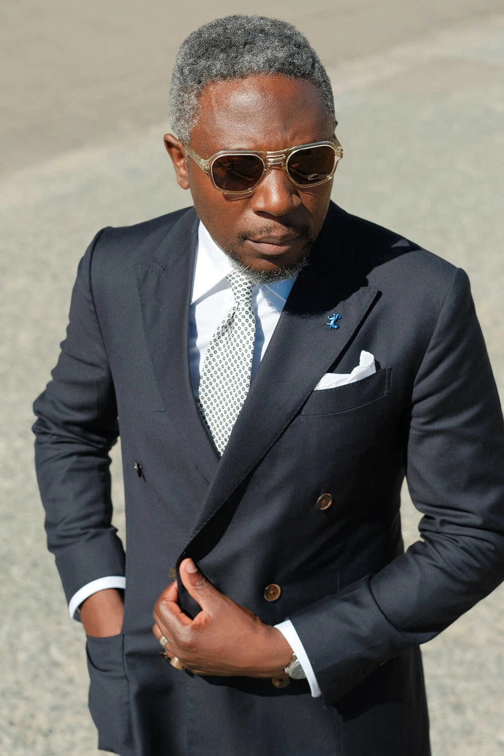 Man in a navy double-breasted suit and sunglasses, street style at Pitti Uomo 100 in Florence