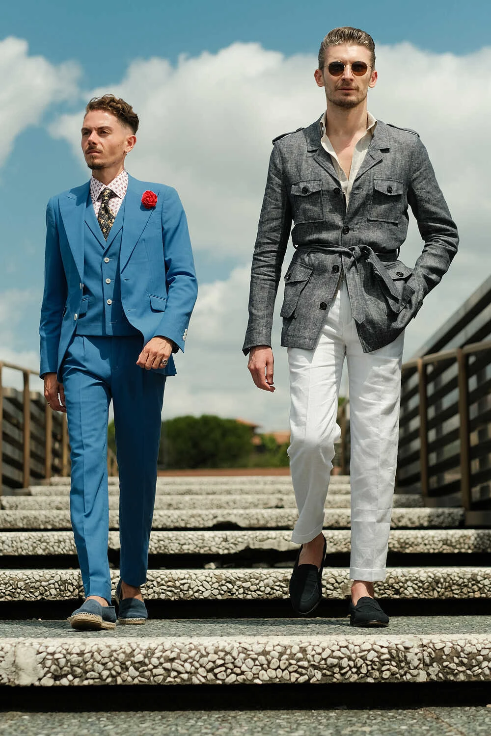 Two models in a blue suit and grey safari jacket on steps for Hockerty in Florence