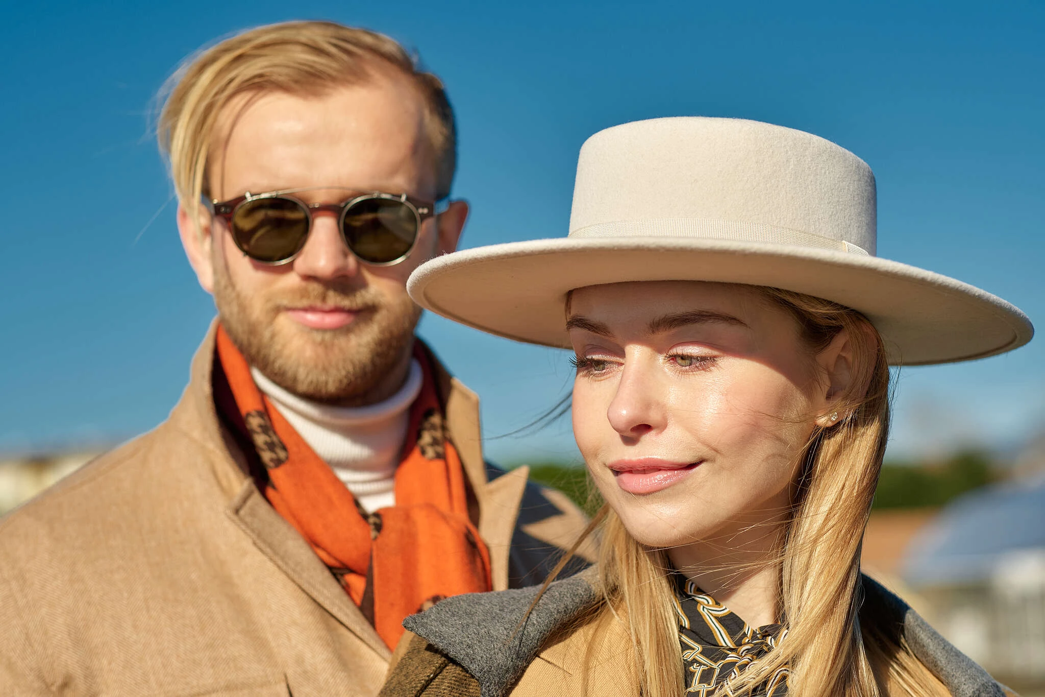 Couple in a camel coat with orange scarf and a cream coat with wide-brim hat, street style at Pitti Uomo 101 in Florence