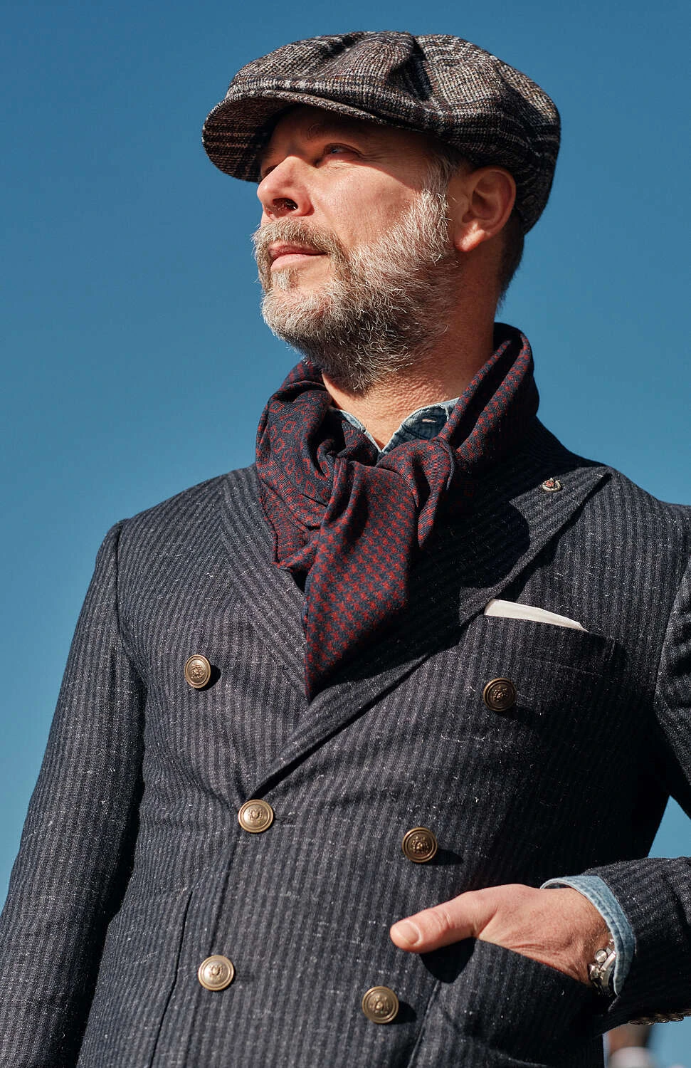 Man in a grey pinstripe jacket, flat cap and cravat, street style at Pitti Uomo 101 in Florence