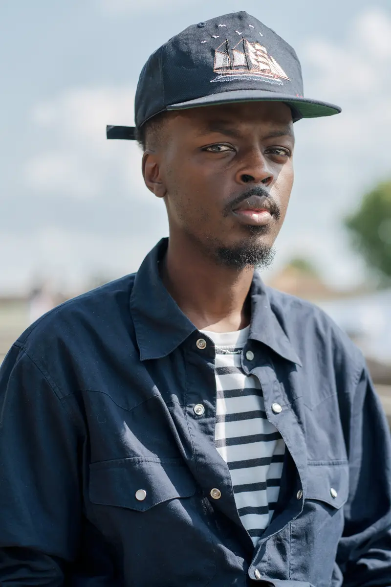 Man in a navy denim shirt over a striped tee and cap, street style at Pitti Uomo 102 in Florence