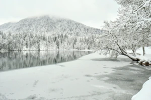 Snowy mountain reflected in the partly frozen Fusine Lake in Friuli Venezia Giulia, winter landscape