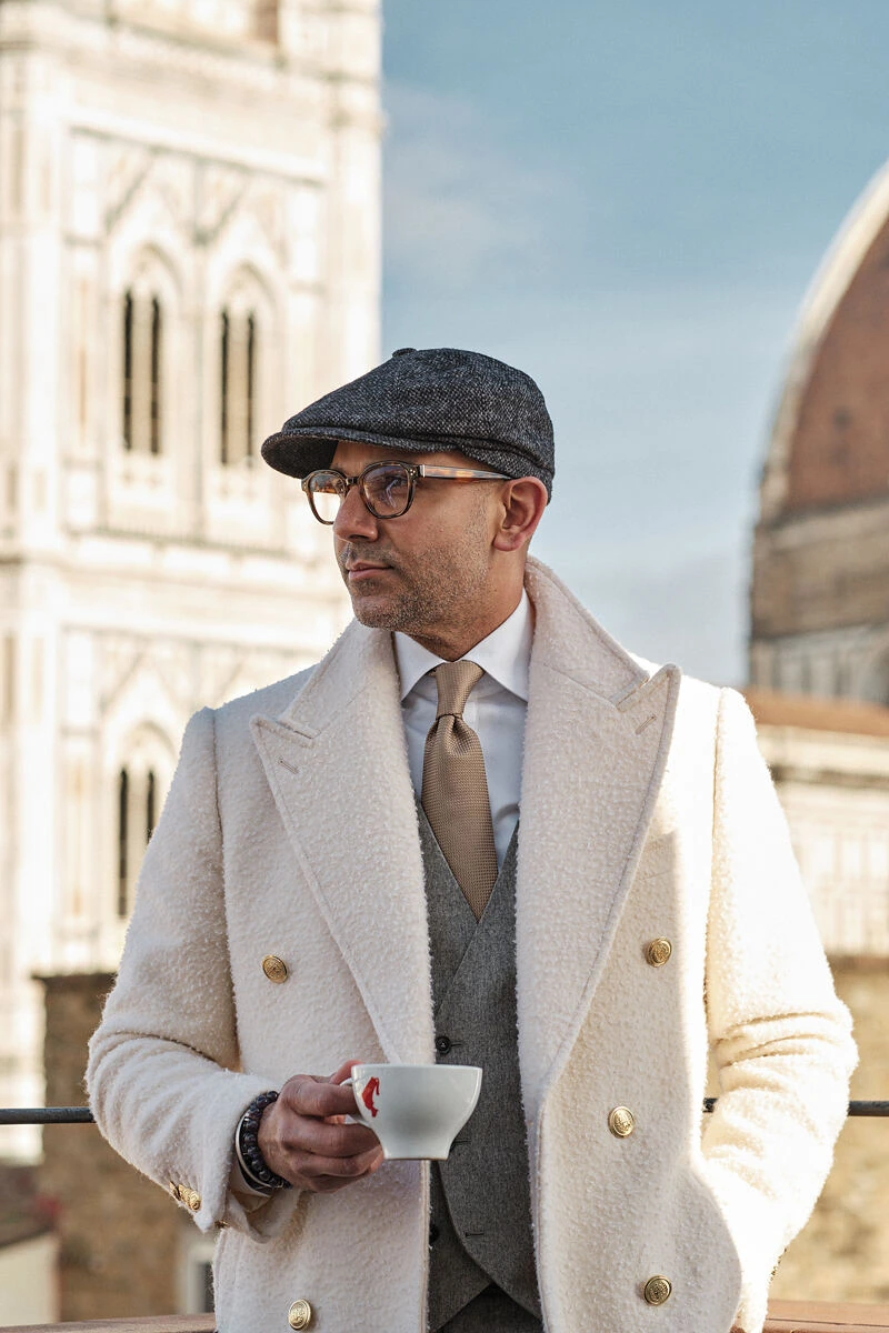 Man in a cream double-breasted coat and flat cap holding an espresso near the Duomo, male fashion street style in Florence