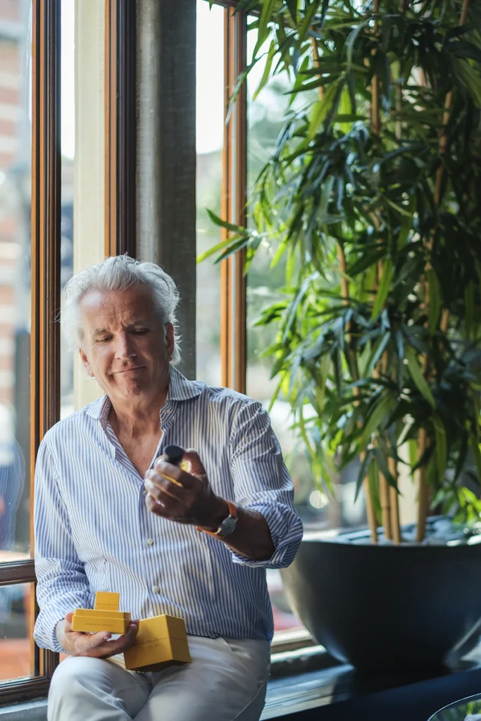 Man holding a YVRA perfume bottle by a window with plants in Amsterdam