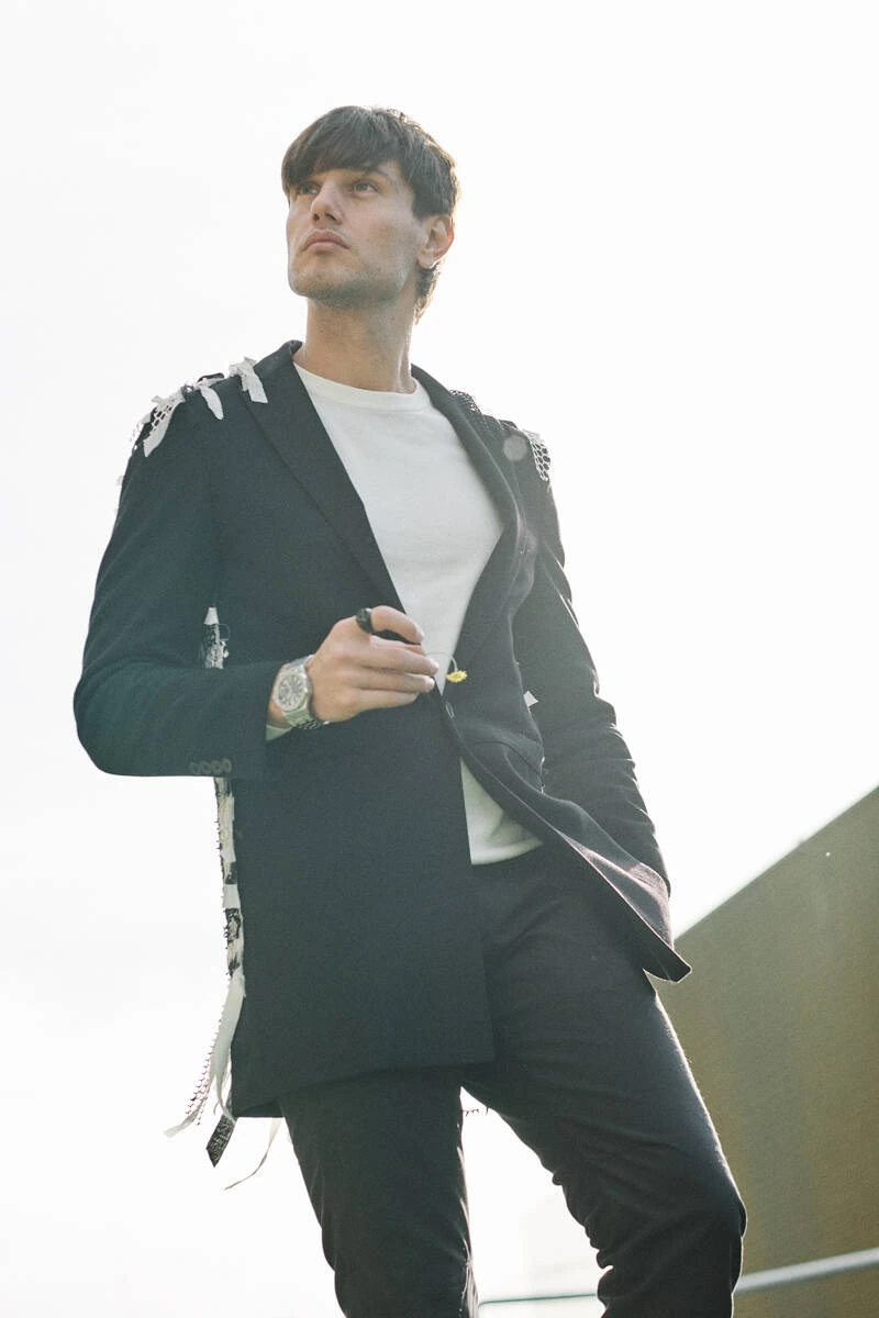 Man in a black suit holding his jacket open over a white tee, street style at Pitti Uomo 103 in Florence