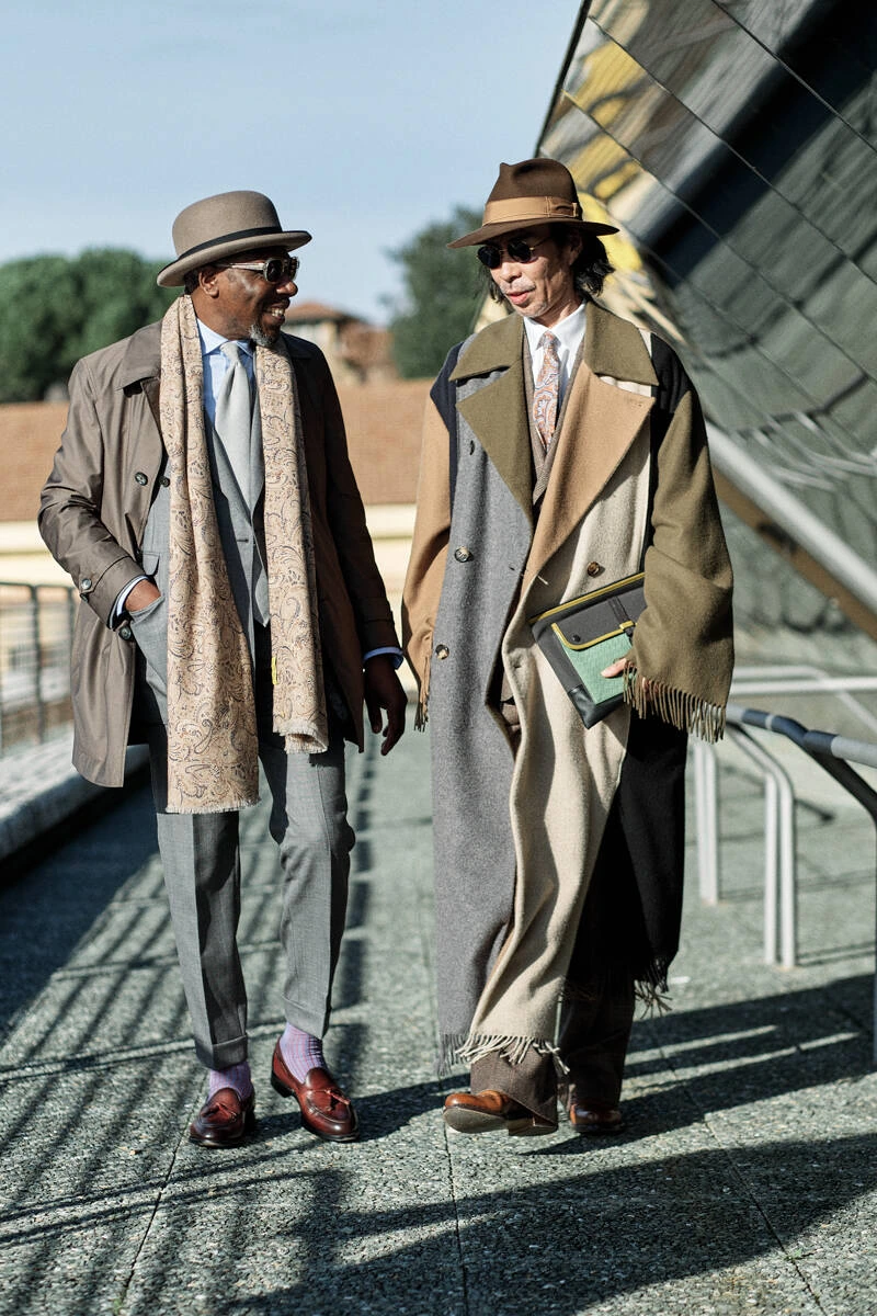 Two men in trench coats and hats on the steps, street style at Pitti Uomo 103 in Florence