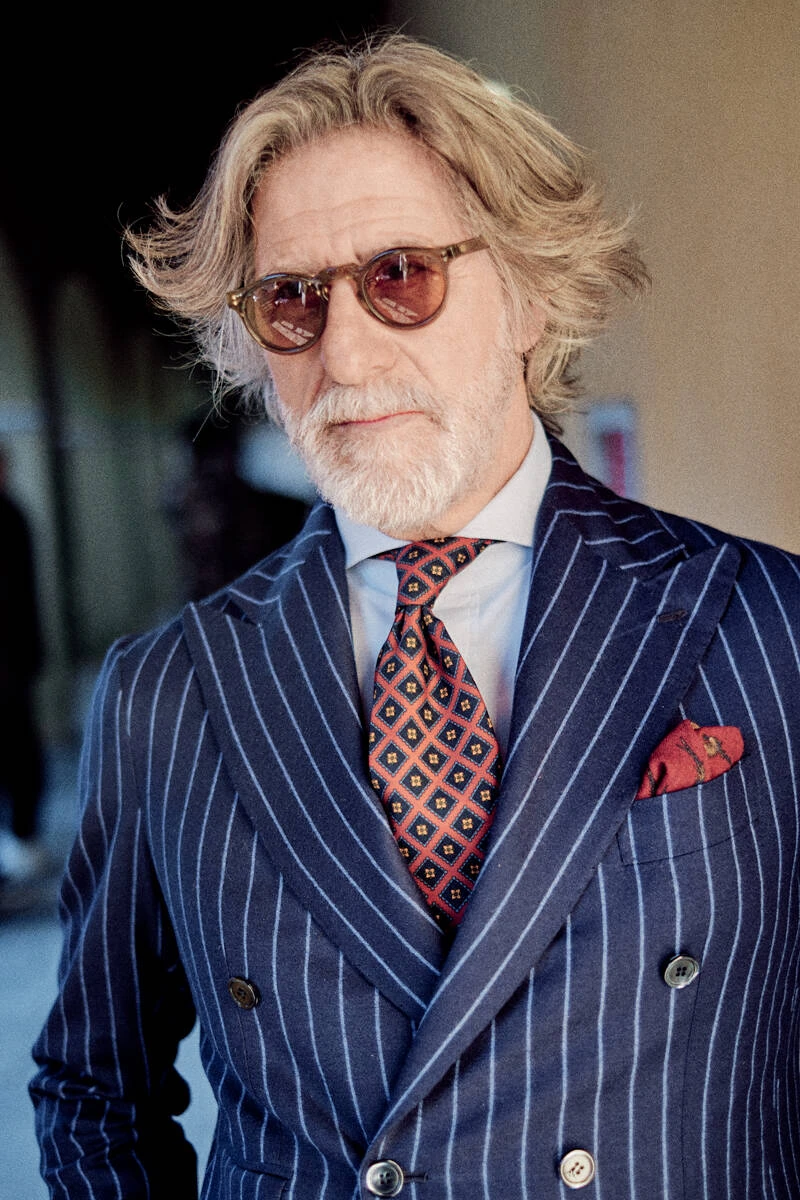 Older man in a navy pinstripe suit with red tie and sunglasses, street style at Pitti Uomo 103 in Florence
