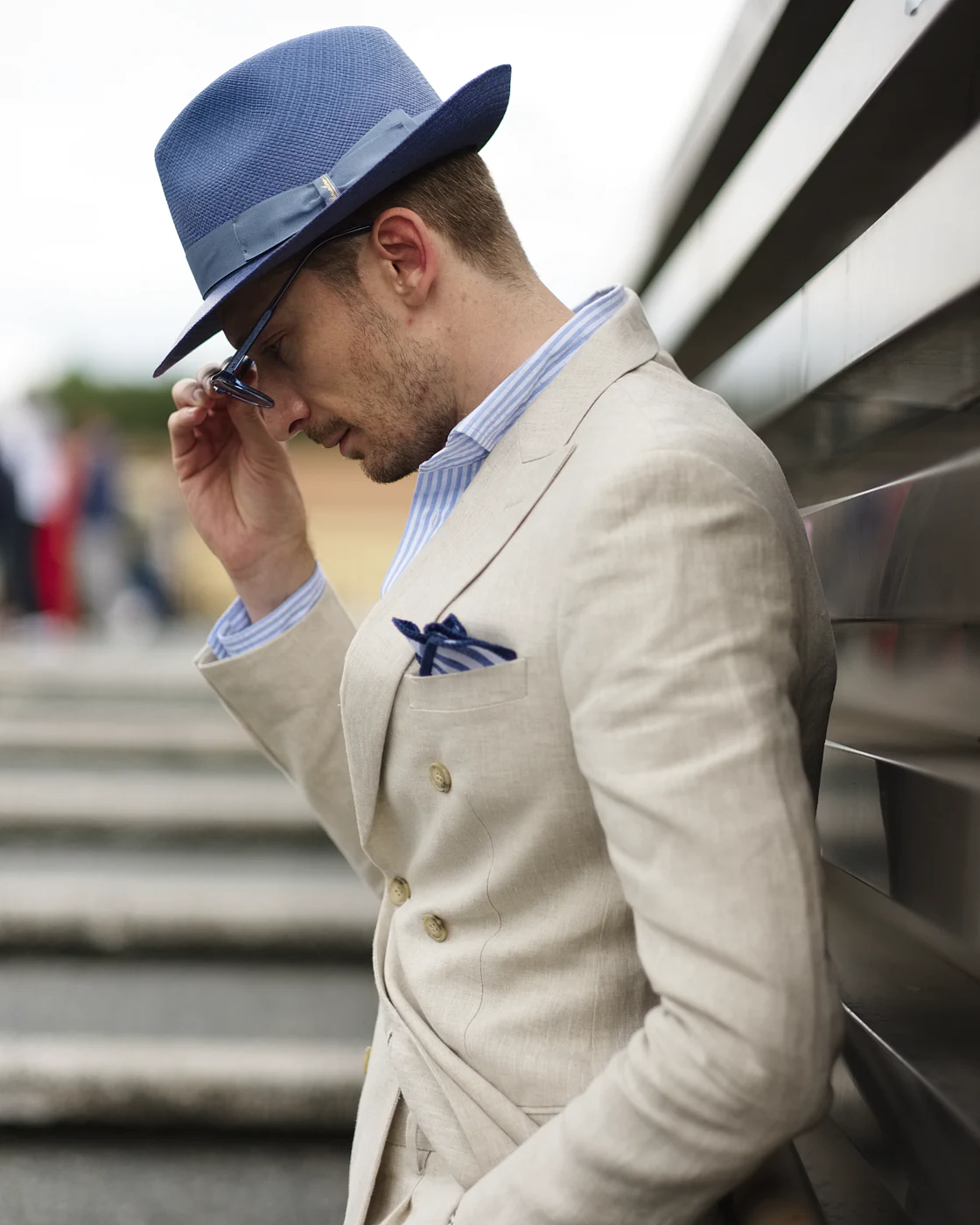 Man in a beige linen suit and navy fedora with a blue striped shirt, street style at Pitti Uomo 104 in Florence