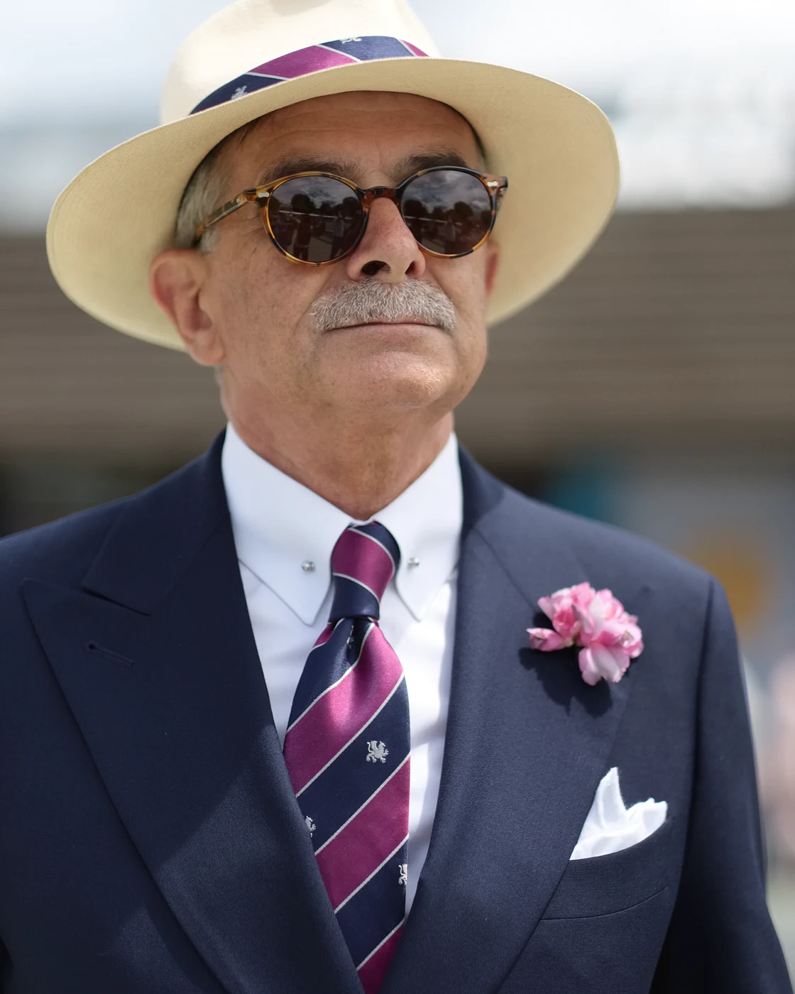 Man in a navy suit with a magenta striped tie and pink boutonniere, street style at Pitti Uomo 104 in Florence
