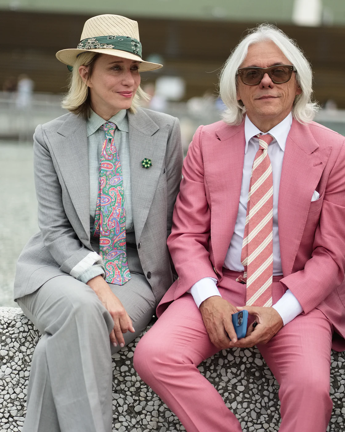 Couple in a grey suit and a pink suit seated on the front row, street style at Pitti Uomo 104 in Florence