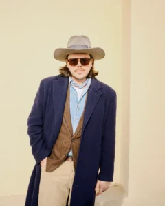 Man in a navy overcoat over a brown cardigan and beige hat, street style at Pitti Uomo 105 in Florence