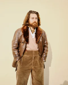 Long-haired man in a fur-collar brown leather jacket and corduroy trousers, street style at Pitti Uomo 105 in Florence