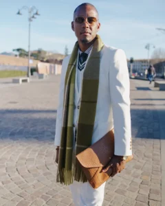 Man in a white suit with a green striped scarf holding a tan clutch, street style at Pitti Uomo 105 in Florence