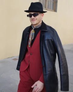 Man in a burgundy three-piece suit under a black leather jacket and fedora, street style at Pitti Uomo 105 in Florence