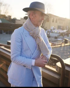 Older man in a light blue suit and grey fedora with a checked scarf, street style at Pitti Uomo 105 in Florence