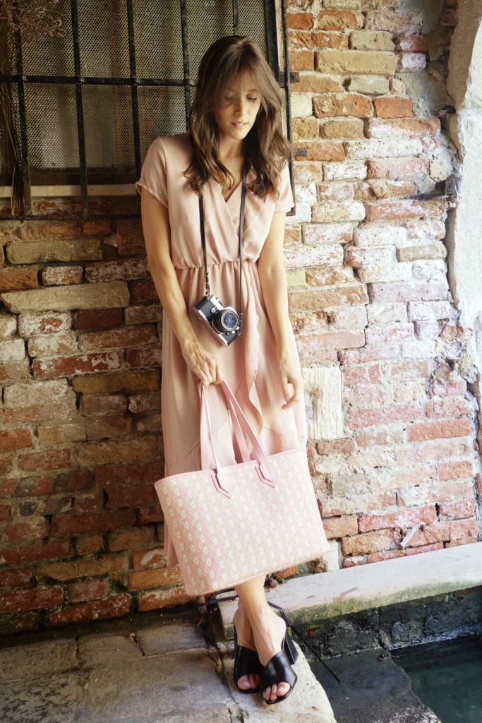 Woman in a blush dress leaning against a Venetian brick wall holding a Vonto pink woven leather tote