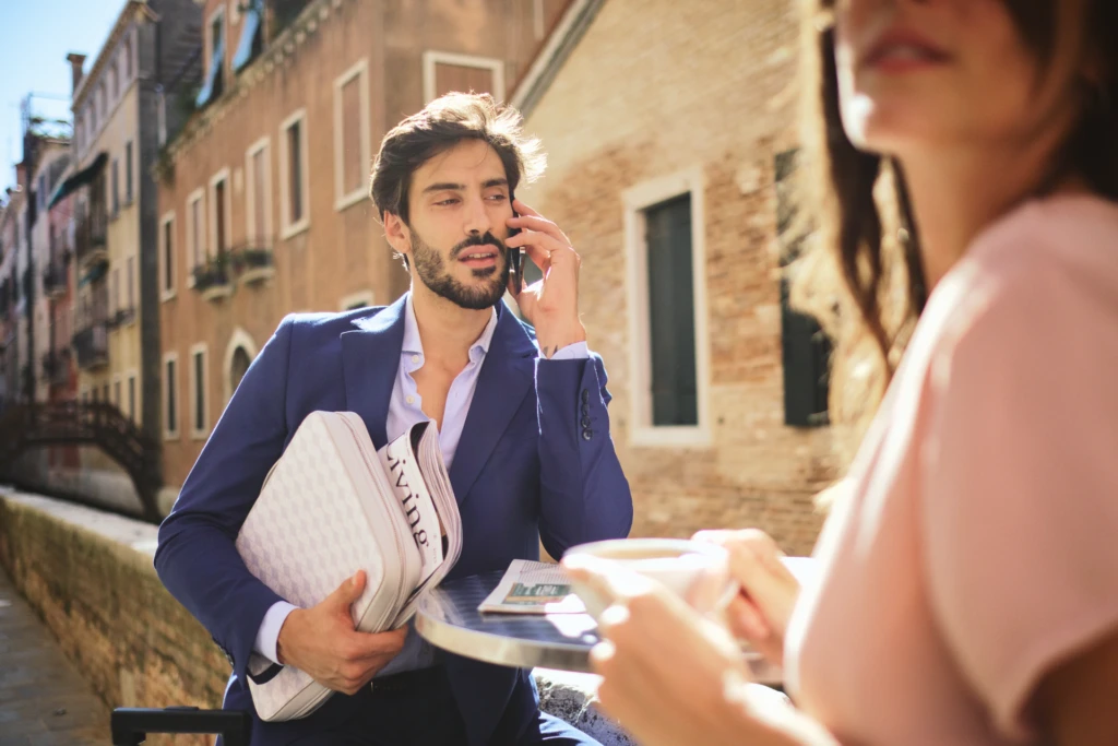 Man on a canal-side terrace holding a Vonto white leather clutch during a Venice lifestyle shoot