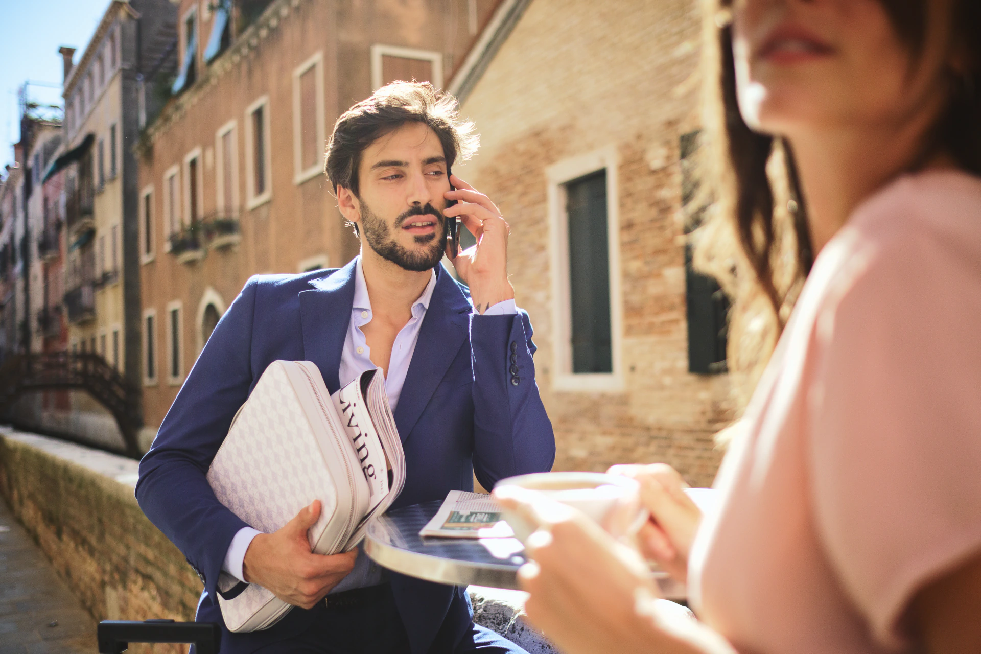 Man on a canal-side terrace holding a Vonto white leather clutch during a Venice lifestyle shoot