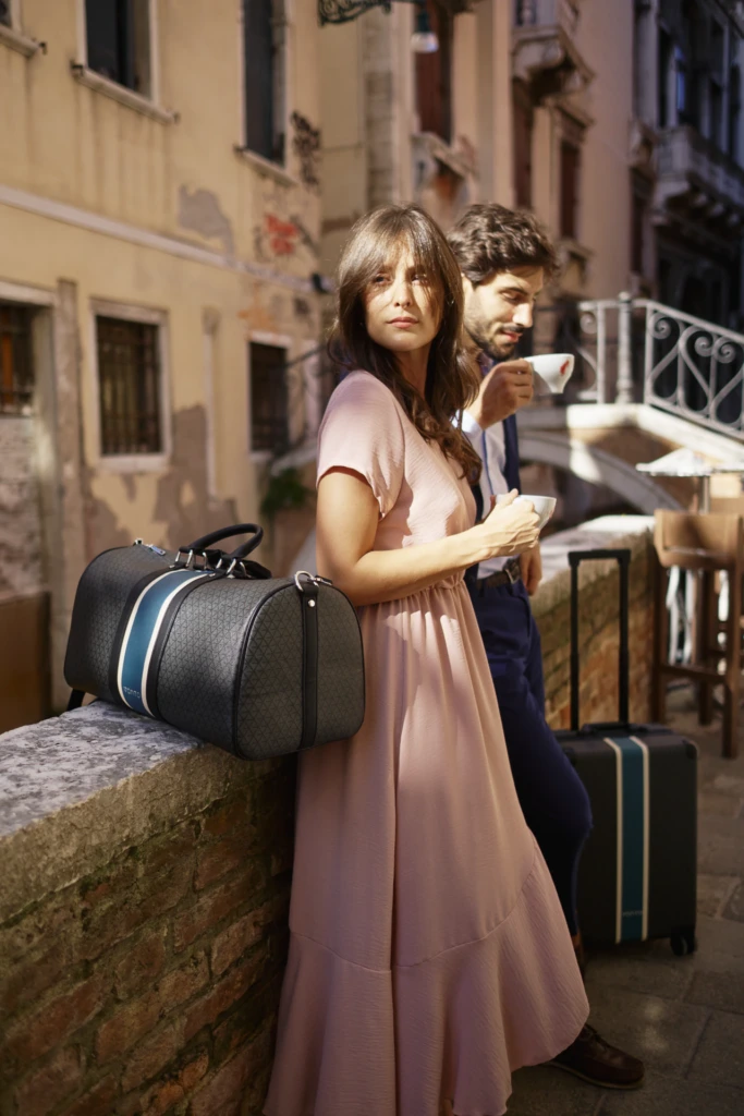Vonto navy leather duffel and rolling suitcase carried by a couple crossing a Venice bridge at dusk