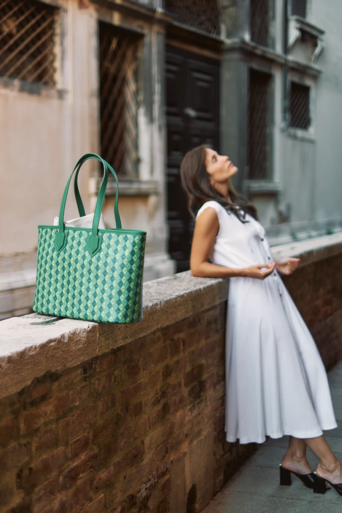 Woman in a white dress leaning on a Venetian wall showcasing a Vonto emerald green leather tote