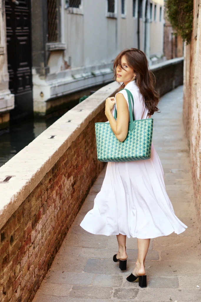 Woman strolling a Venice canal walkway with a Vonto green woven leather tote over her shoulder