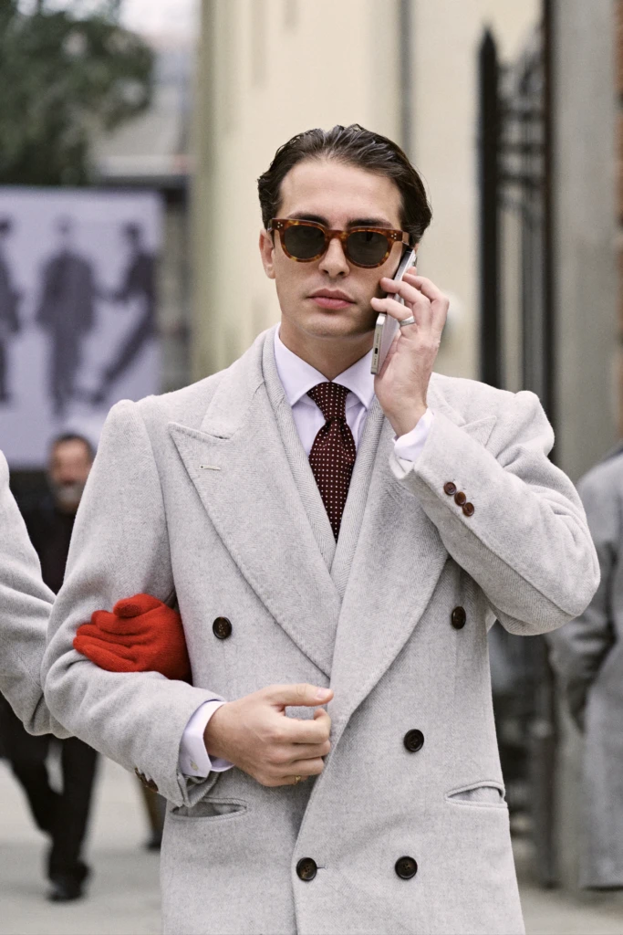 Young man on the phone in a cream herringbone double-breasted coat with a burgundy polka-dot tie and red gloves, Pitti Immagine Uomo 109