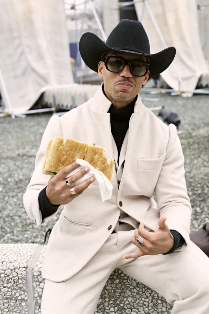 Man in a cream wool suit and black cowboy hat eating a sandwich at the Pitti Immagine Uomo 109 fair, Florence