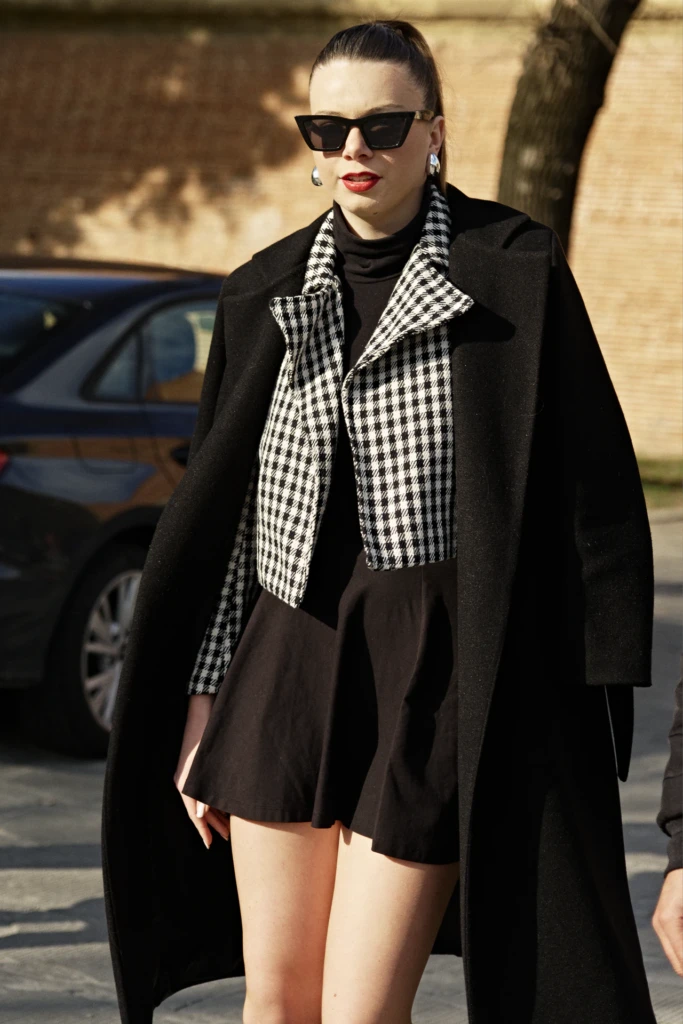 Woman in oversized black coat, black-and-white checked jacket and cat-eye sunglasses at Pitti Immagine Uomo 107 — Florence womenswear street style.