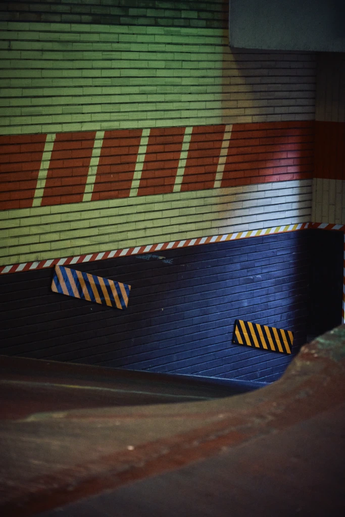 Detail of a graffiti-covered roller shutter with colorful striped brickwork and hazard tape at a Milano street corner
