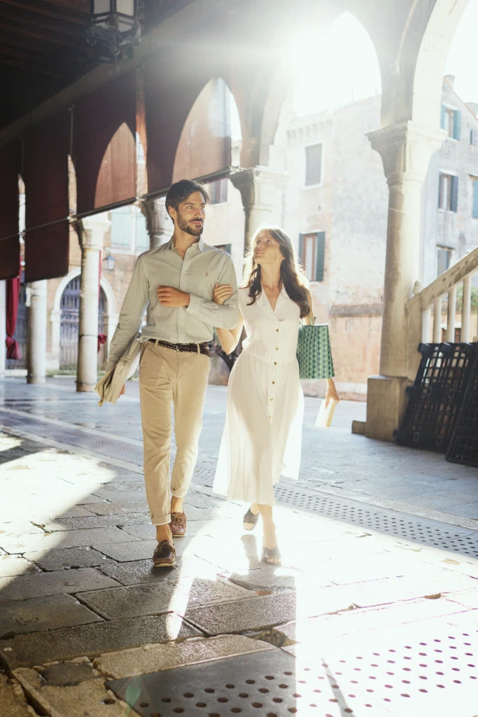 Sunlit couple strolling through a Venetian arcade with a Vonto leather briefcase and green tote