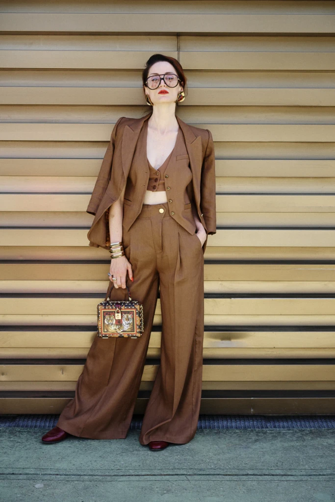 Woman in a tailored brown suit with gold jewelry and a tiger-print handbag at Pitti Uomo, Florence