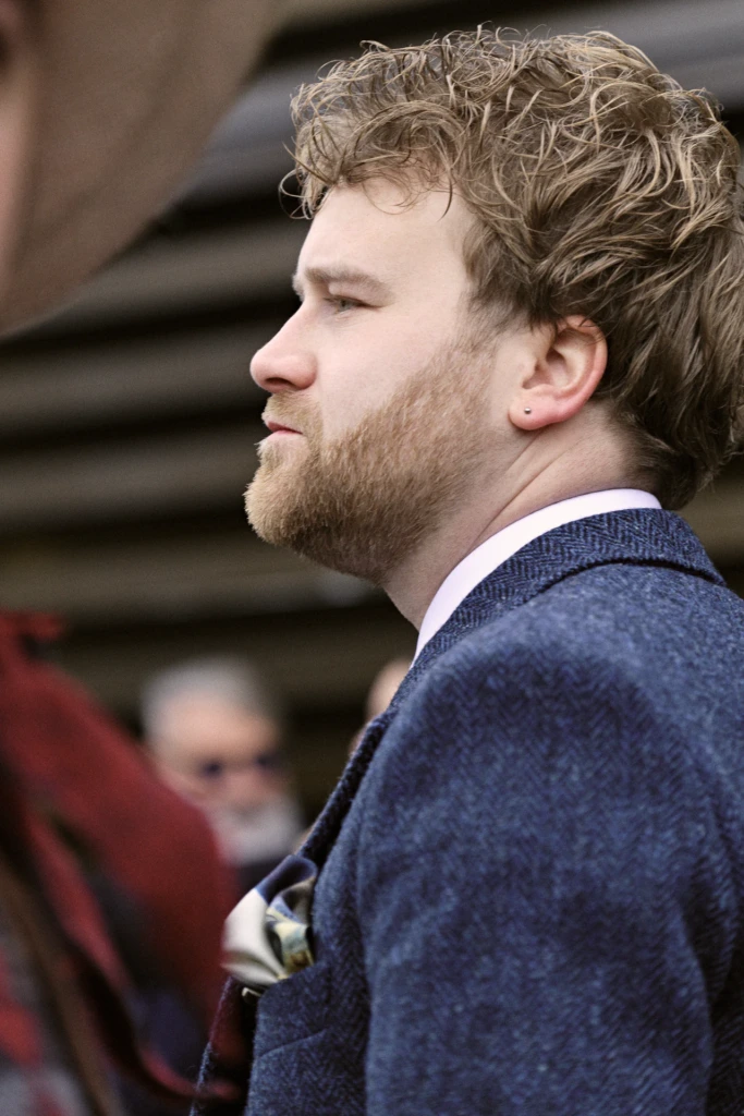 Young man in profile with a red beard and earring, wearing a navy herringbone coat, Pitti Immagine Uomo 109 fair, Florence