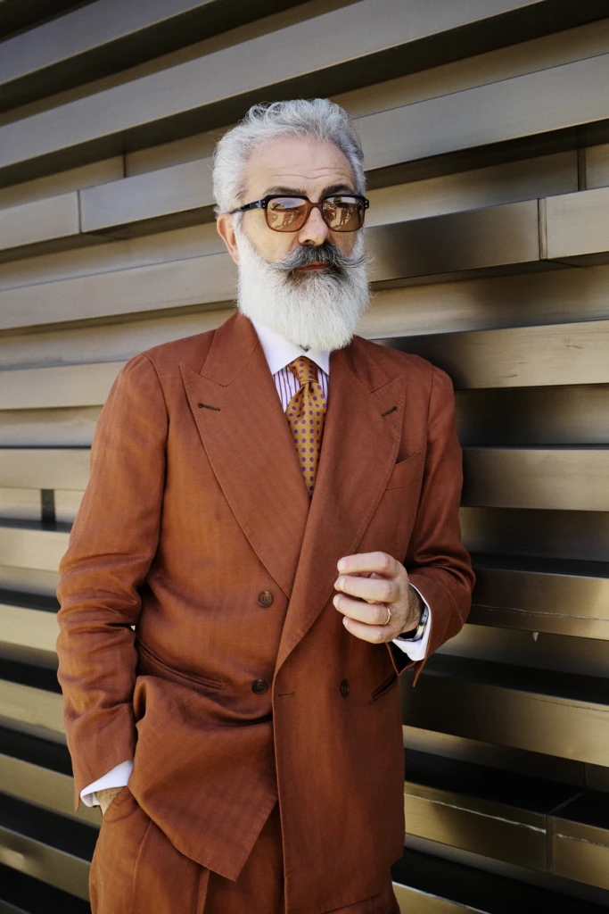Older man with a white beard and tortoiseshell glasses in a rust double-breasted suit with a polka dot tie at Pitti Immagine Uomo 110