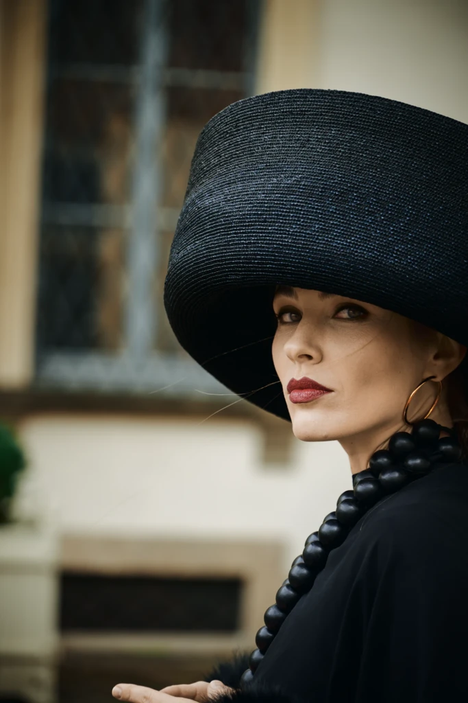 Woman in a wide-brim black hat and chunky black beaded necklace, gold hoop earring and bold red lipstick, Milano Fashion Week street style portrait