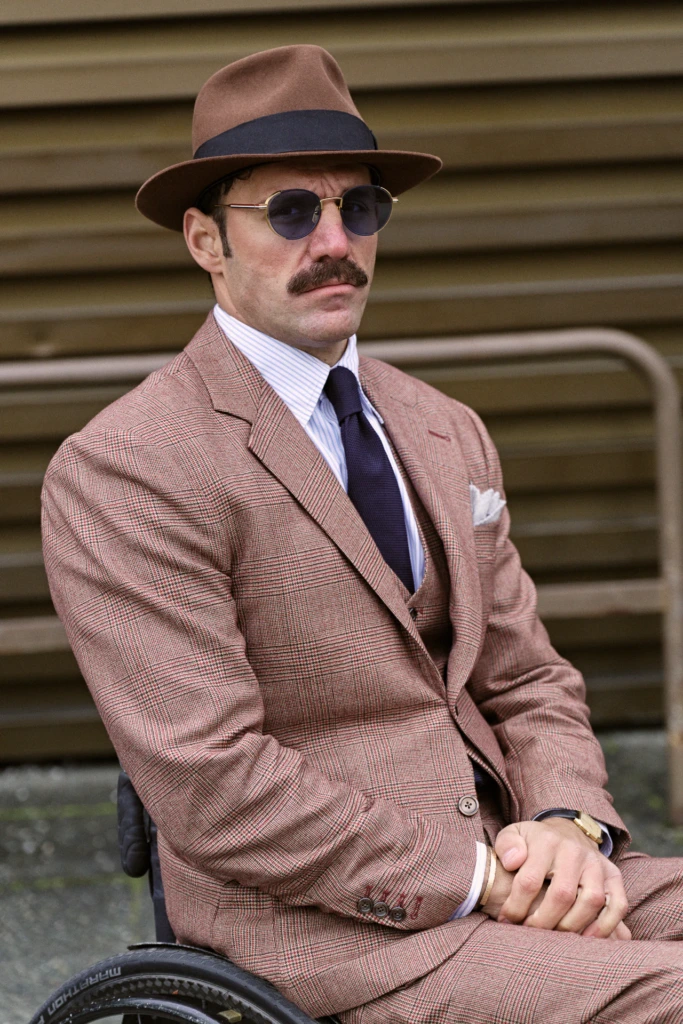 Man in a wheelchair wearing a brown houndstooth three-piece suit and trilby hat, Pitti Immagine Uomo 109 fair, Florence