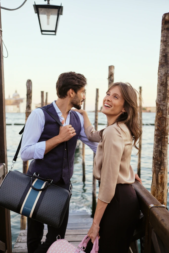 Vonto navy striped leather duffel and pink pouch styled with a couple beside a Venice lagoon dock