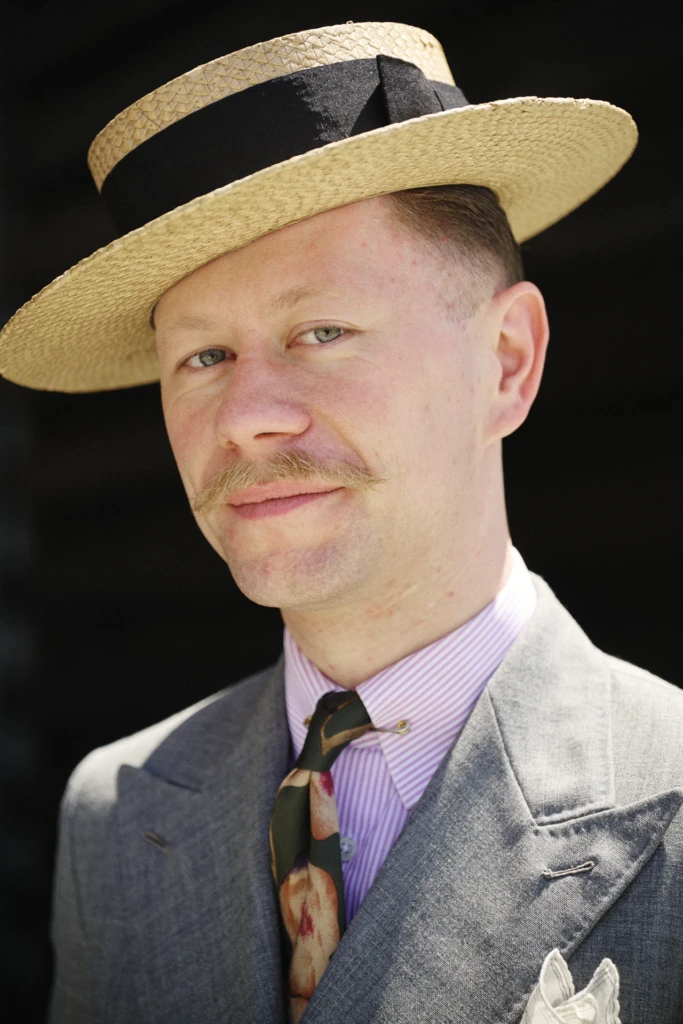 Man in a gray suit wearing a straw boater hat and a camouflage-print tie at Pitti Immagine Uomo 110